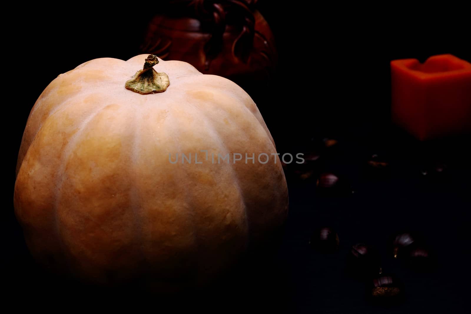 Pumpkin. Chestnuts and candle in background. Dark background