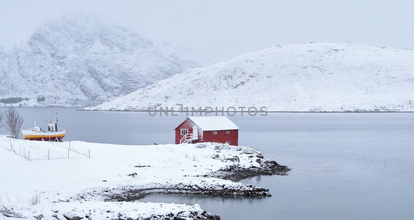 Panorama of traditional red rorbu house and fjord shore with heavy snow in winter. Lofoten islands, Norway