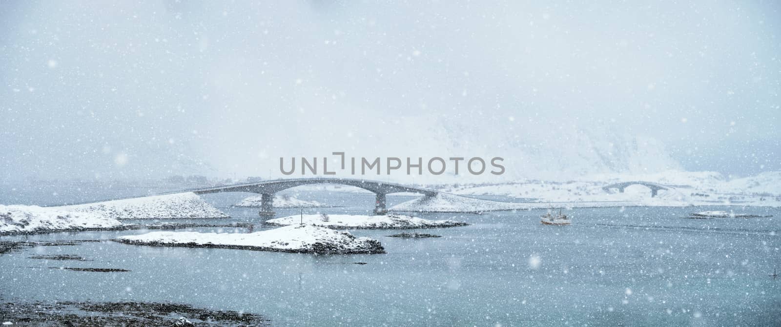 Fredvang bridges in heavy snowfall in winter with fishing ship. Lofoten islands, Norway
