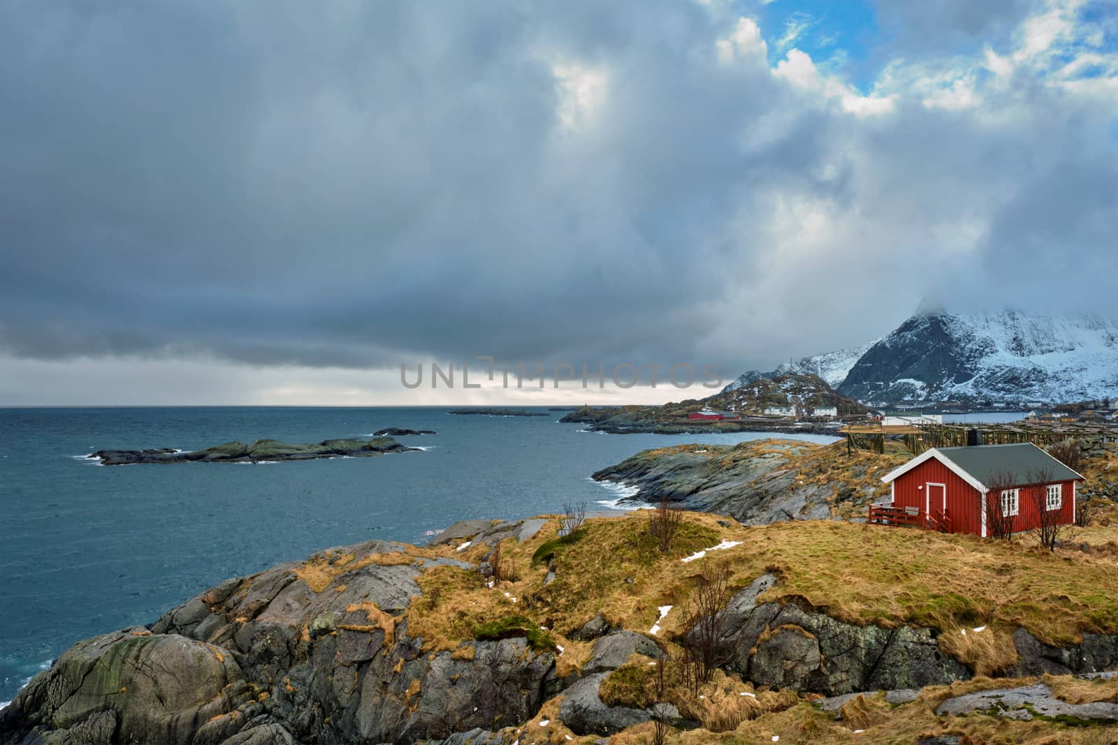 Clif with traditional red rorbu house on Litl-Toppoya islet on Lofoten Islands, Norway in winter