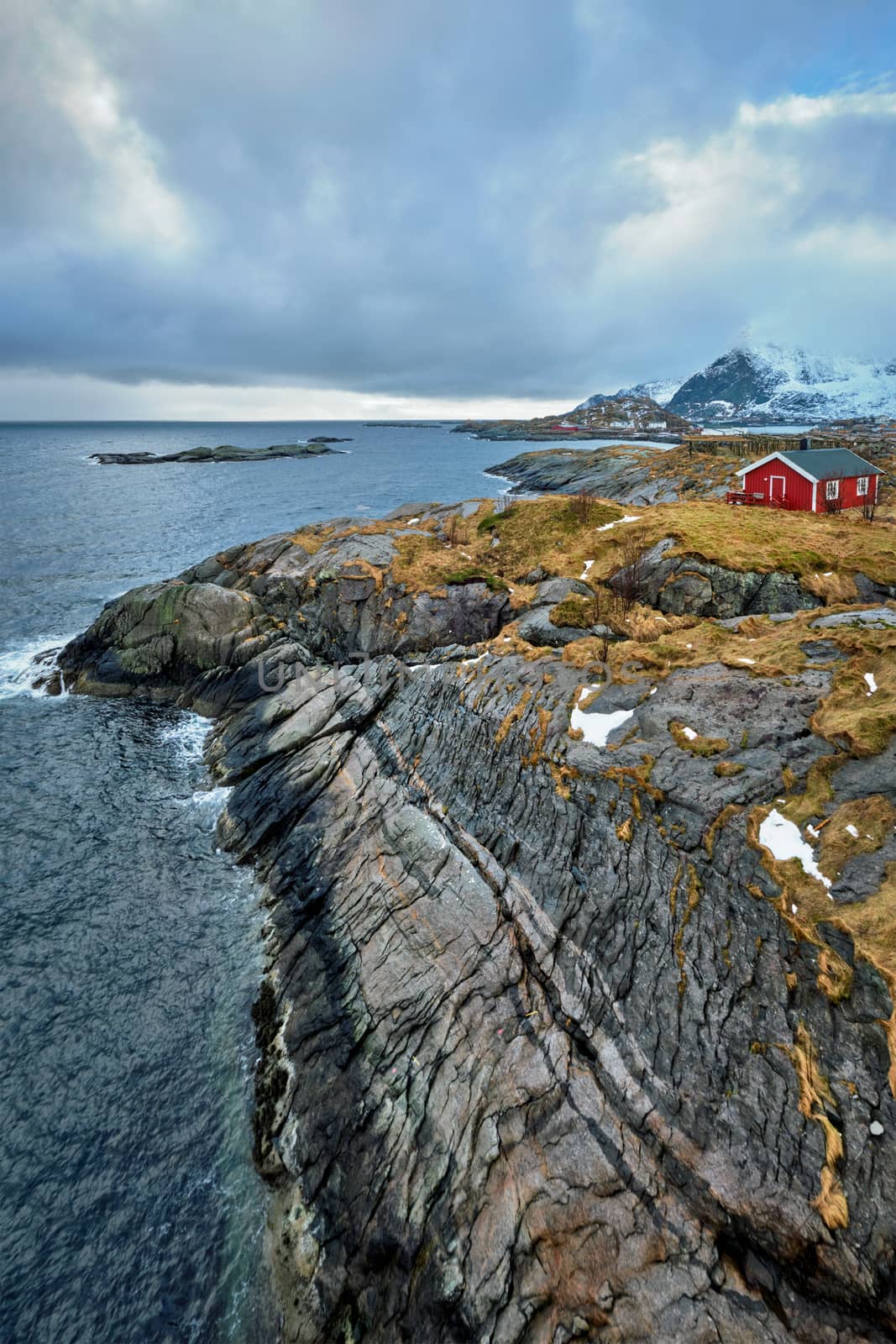 Clif with traditional red rorbu house on Litl-Toppoya islet on Lofoten Islands, Norway in winter