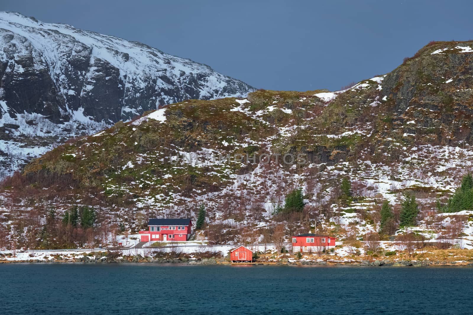 Traditional red rorbu houses on fjord shore in snow in winter. Lofoten islands, Norway