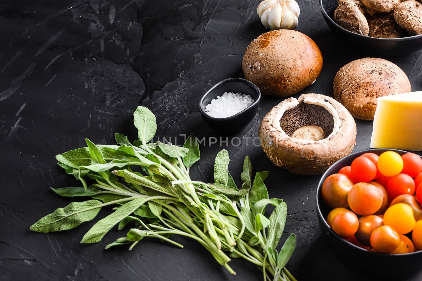 Portabello mushrooms ingredients for baking, cheddar cheese and sage on black background. Side view.