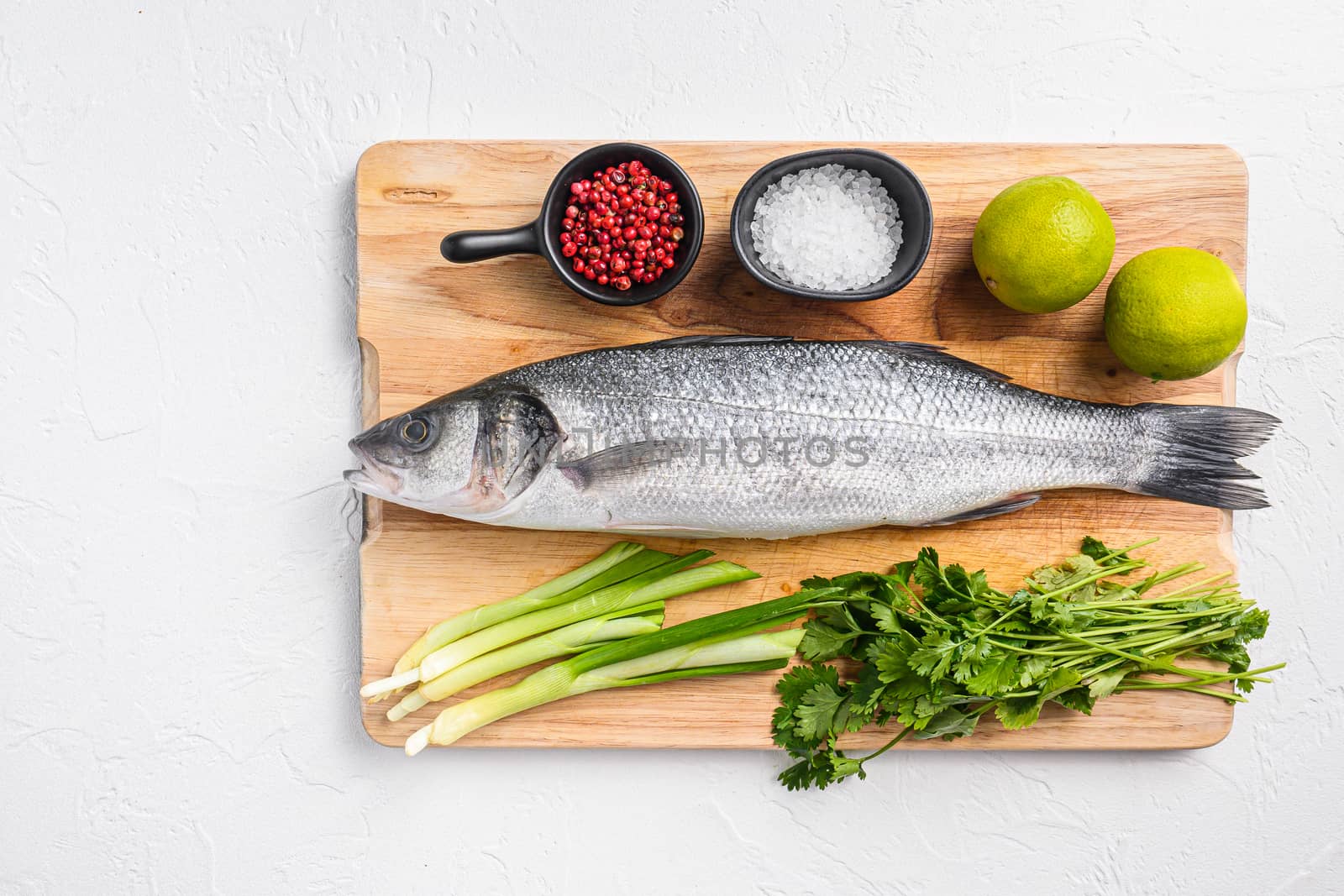 Whole sea bass with spices and herbs ingredients on chopping board over white textured background top view space for text