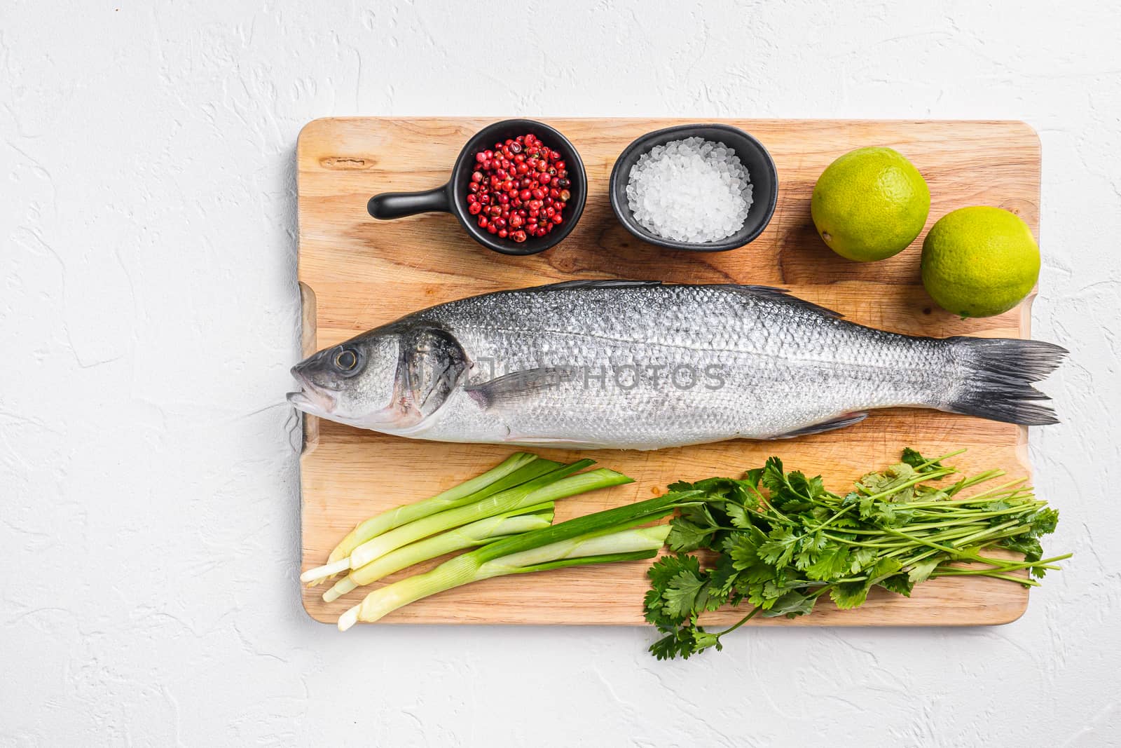 Whole sea bass with spices and herbs ingredients on chopping board over white textured background top view space for text. by Ilianesolenyi