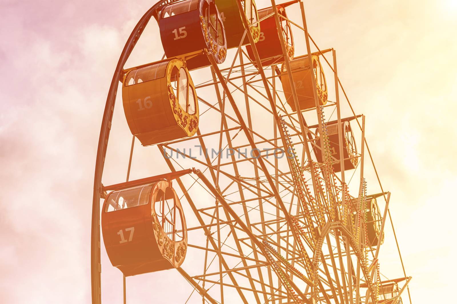 Ferris wheel with multi-colored cabs against the sky with clouds and sunbeams in the park on a sunny spring day.