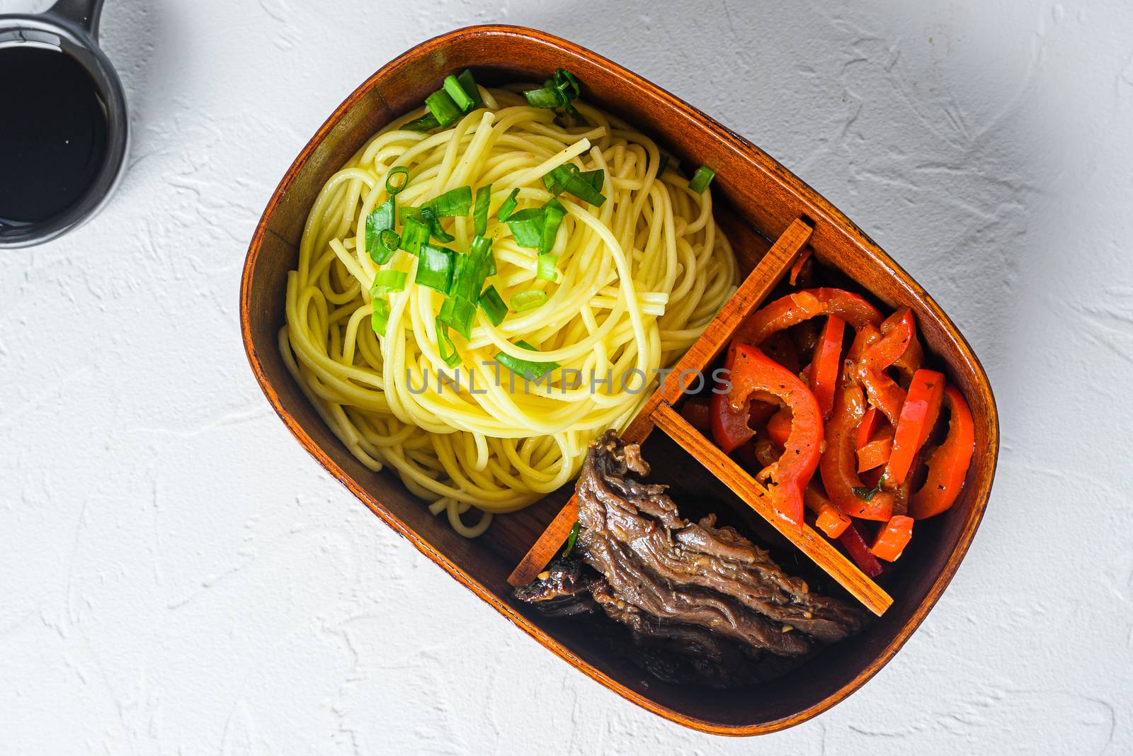 Bento beef noodles lunch box top view on white table close up.