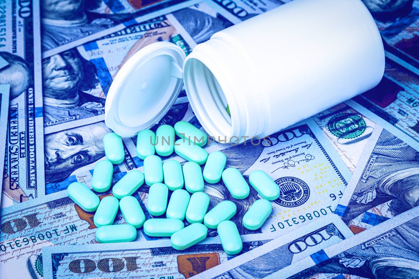 Green pills on the background of one hundred dollar bills. The concept of the expensive cost of healthcare or financing medicine. White medicine bottle with copy space for text.