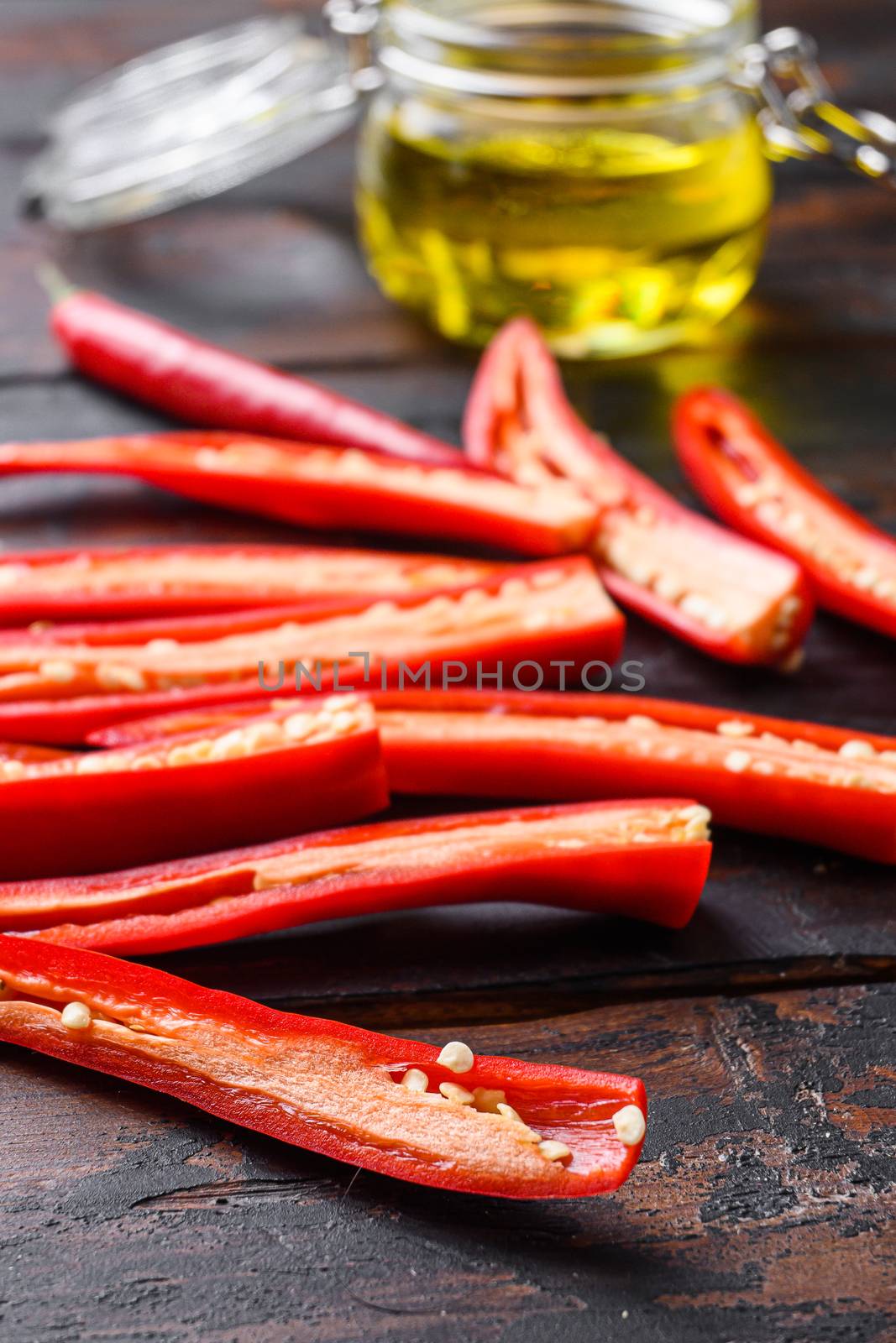 Ripe chili pepper sliced for making spicy olive oil over old dark wooden table side view selective focus. by Ilianesolenyi