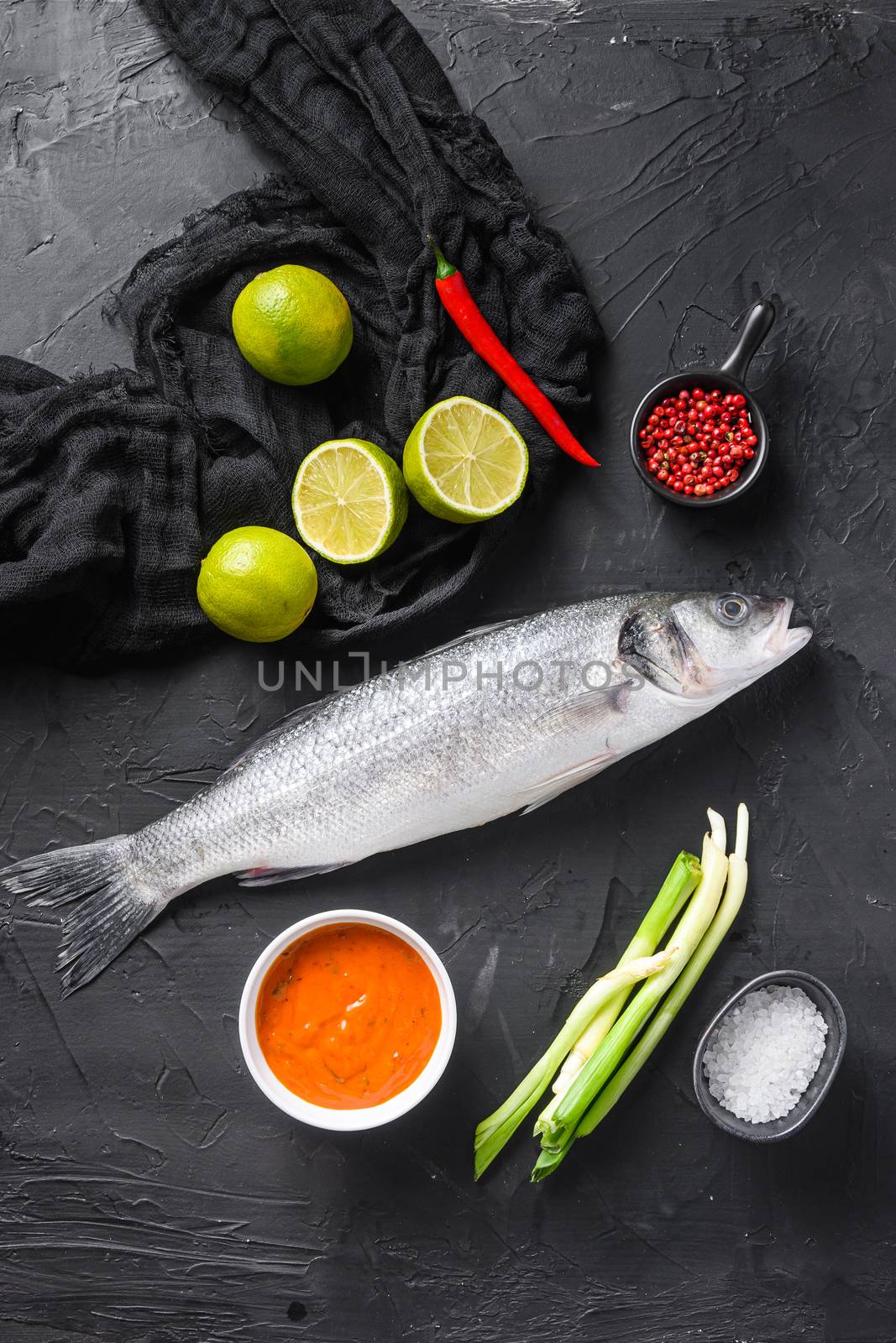 Raw seabass with spices and herbs ingredients on black background top view