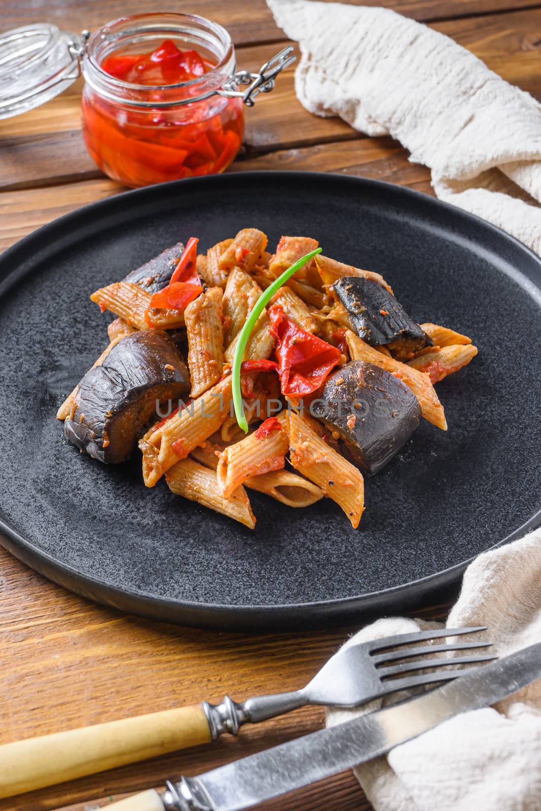 Aubergine penne eggplant pasta, pepper tomatoe sauce, on black plate over wooden table served side view close up by Ilianesolenyi