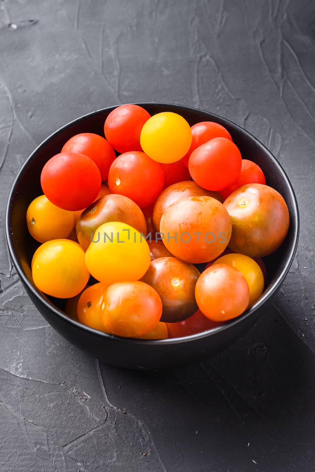 Cherry tomatoes in bowl on black background side view