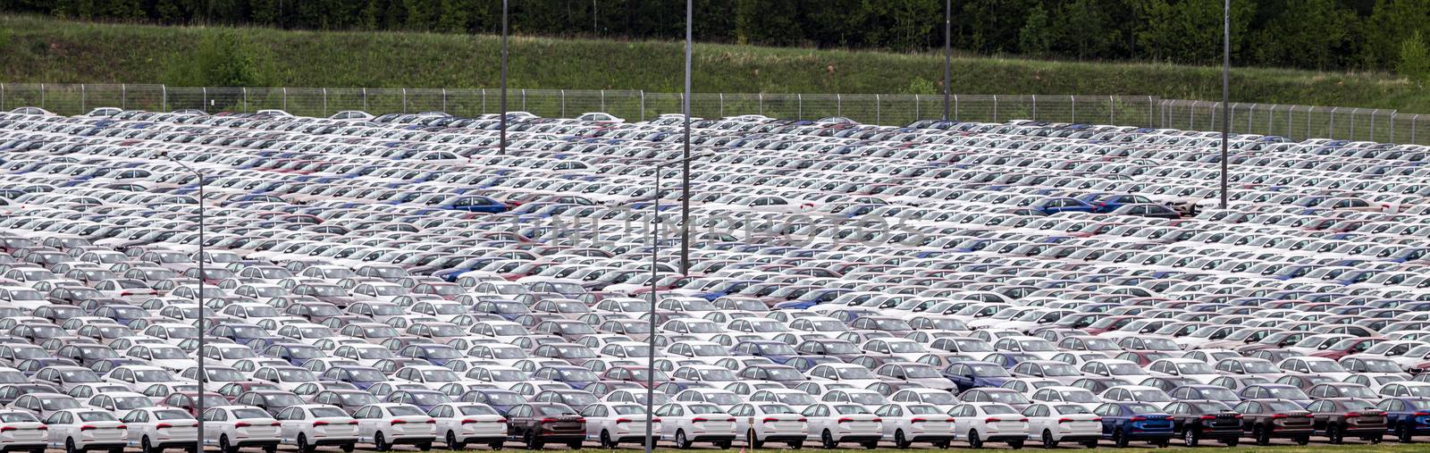 Rows of a new cars parked in a distribution center on a cloudy day in the spring, a car factory. Top view to the parking in the open air. by Eugene_Yemelyanov