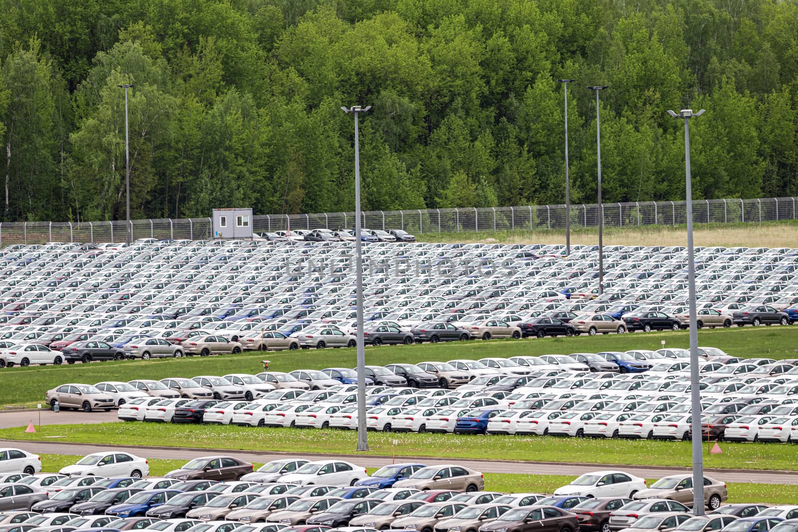 Rows of a new cars parked in a distribution center on a car factory on a cloudy day. Top view to the parking in the open air. by Eugene_Yemelyanov