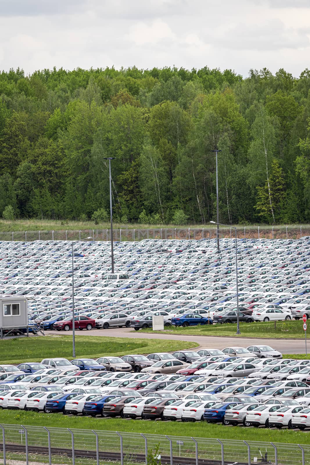 Rows of a new cars parked in a distribution center on a cloudy day in the spring, a car factory. Top view to the parking in the open air. by Eugene_Yemelyanov