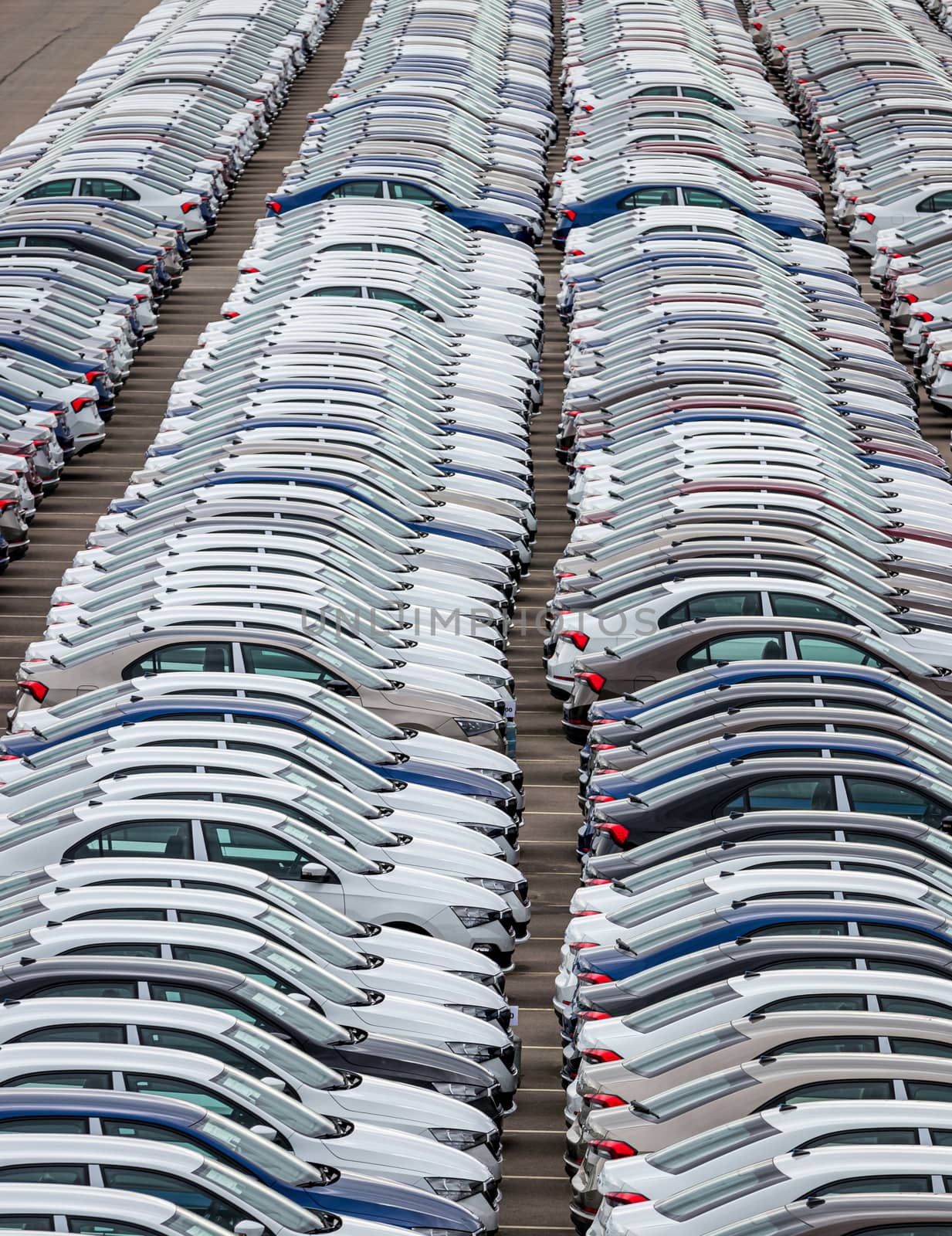 Rows of a new cars parked in a distribution center on a cloudy day in the spring, a car factory. Top view to the parking in the open air.