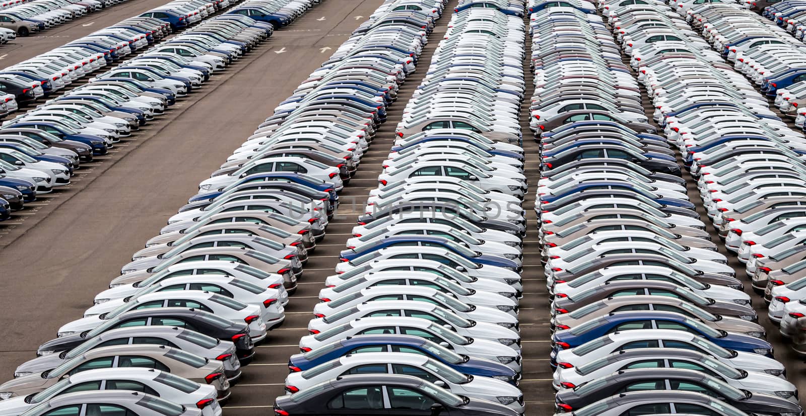 Rows of a new cars parked in a distribution center on a car factory on a cloudy day. Top view to the parking in the open air. by Eugene_Yemelyanov