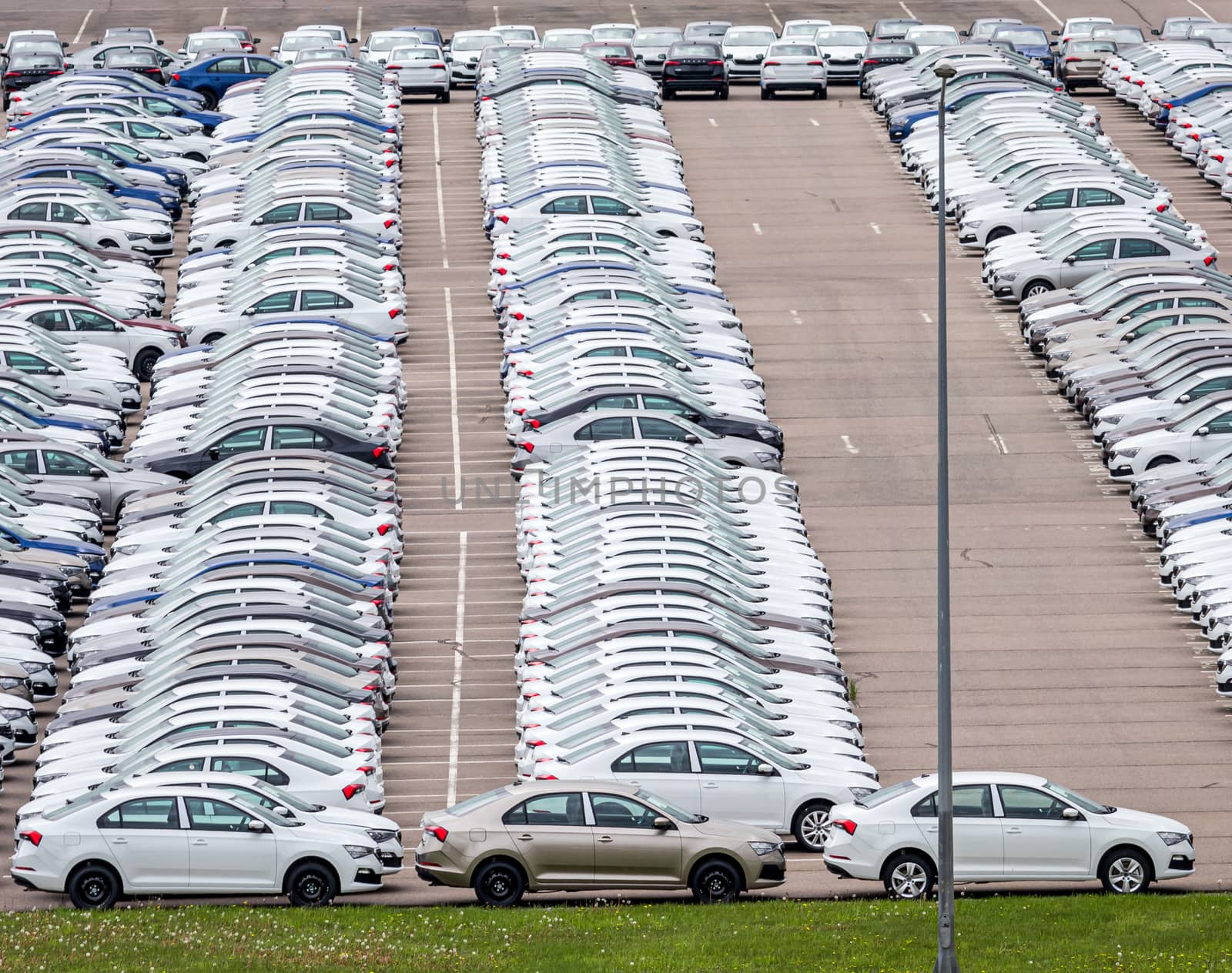 Rows of a new cars parked in a distribution center on a car factory on a cloudy day. Top view to the parking in the open air.