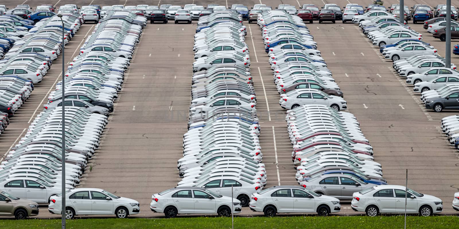 Rows of a new cars parked in a distribution center on a cloudy day in the spring, a car factory. Top view to the parking in the open air. by Eugene_Yemelyanov