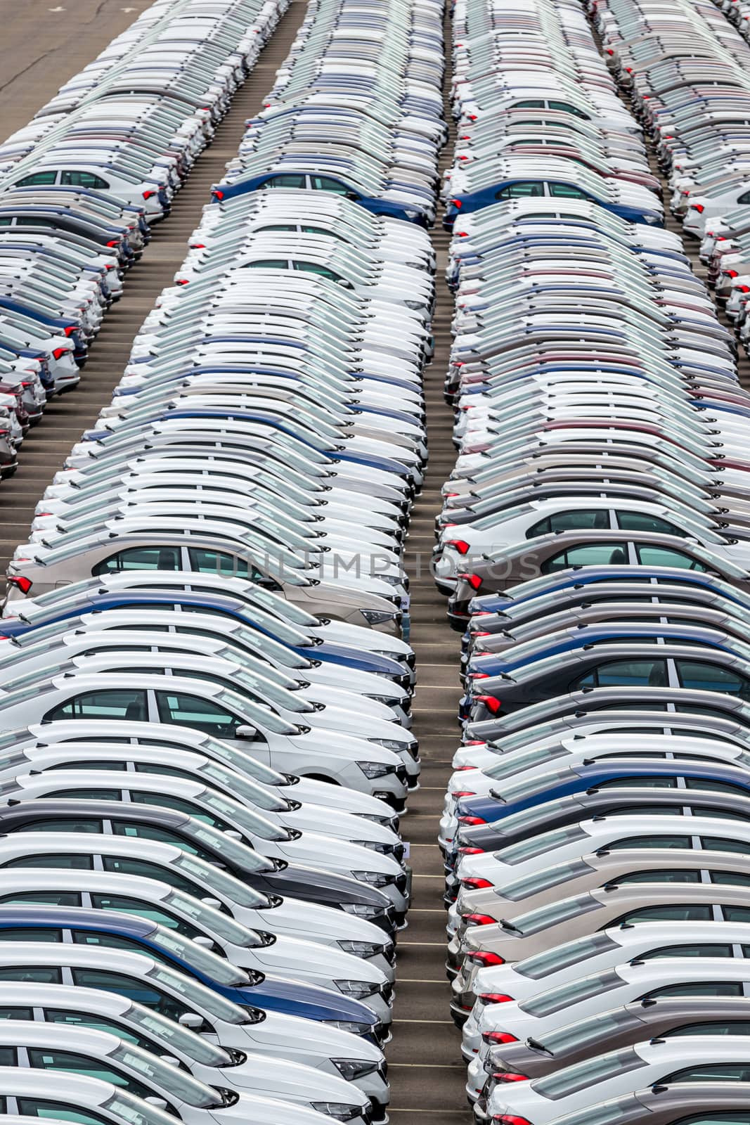 Rows of a new cars parked in a distribution center on a car factory on a cloudy day. Top view to the parking in the open air. by Eugene_Yemelyanov