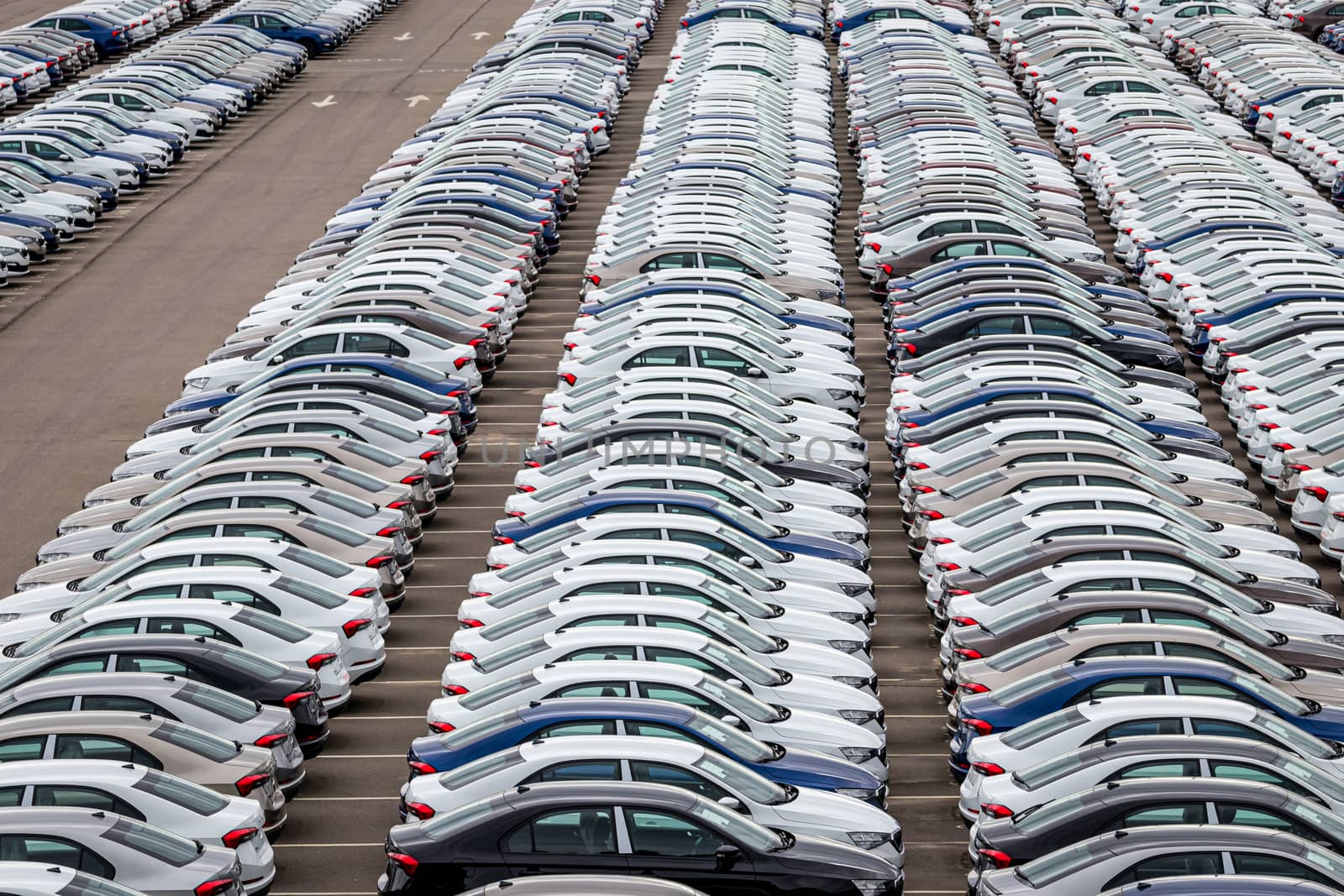 Rows of a new cars parked in a distribution center on a cloudy day in the spring, a car factory. Top view to the parking in the open air. by Eugene_Yemelyanov