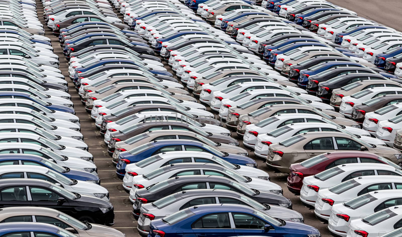 Rows of a new cars parked in a distribution center on a cloudy day in the spring, a car factory. Top view to the parking in the open air.