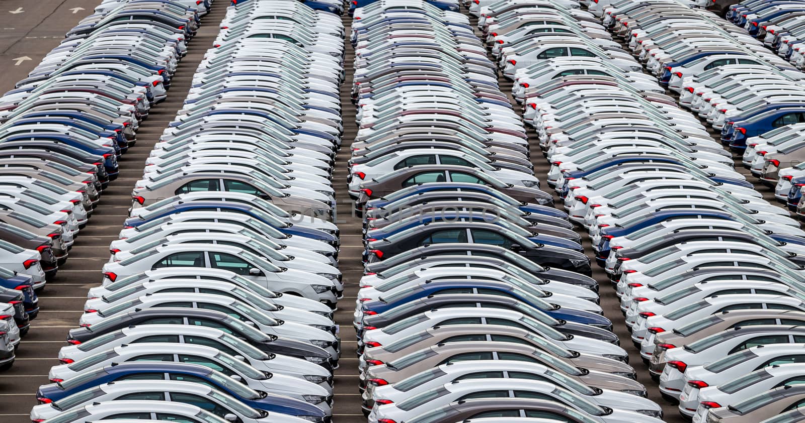 Rows of a new cars parked in a distribution center of a car factory. Top view to the parking in the open air.