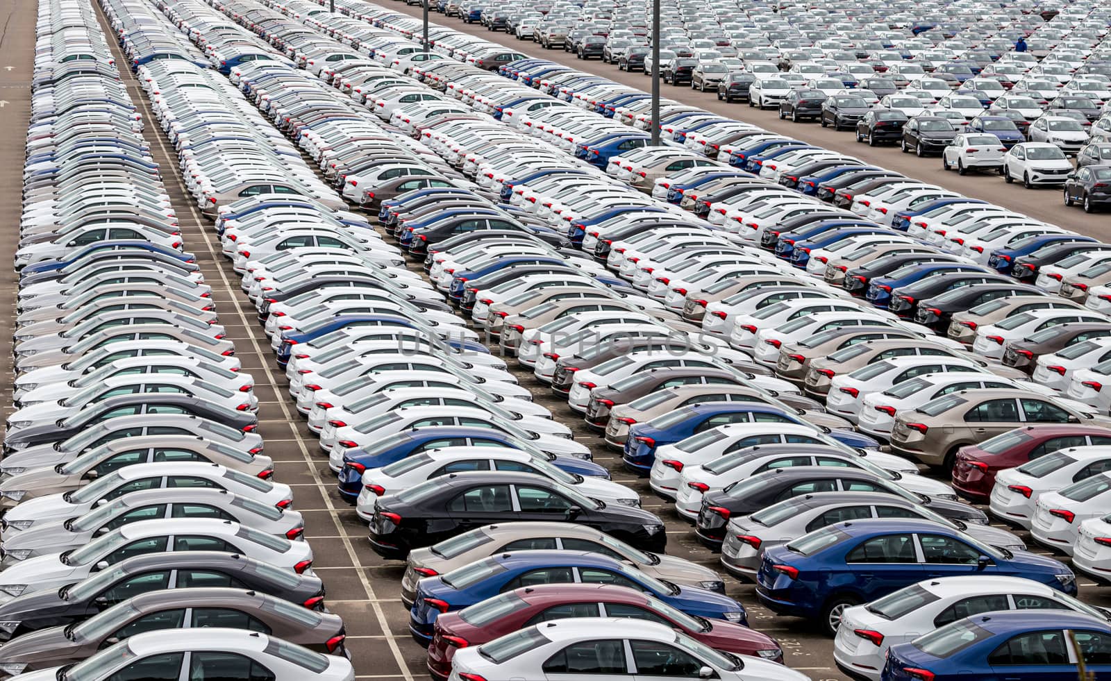 Rows of a new cars parked in a distribution center on a cloudy day in the spring, a car factory. Top view to the parking in the open air.