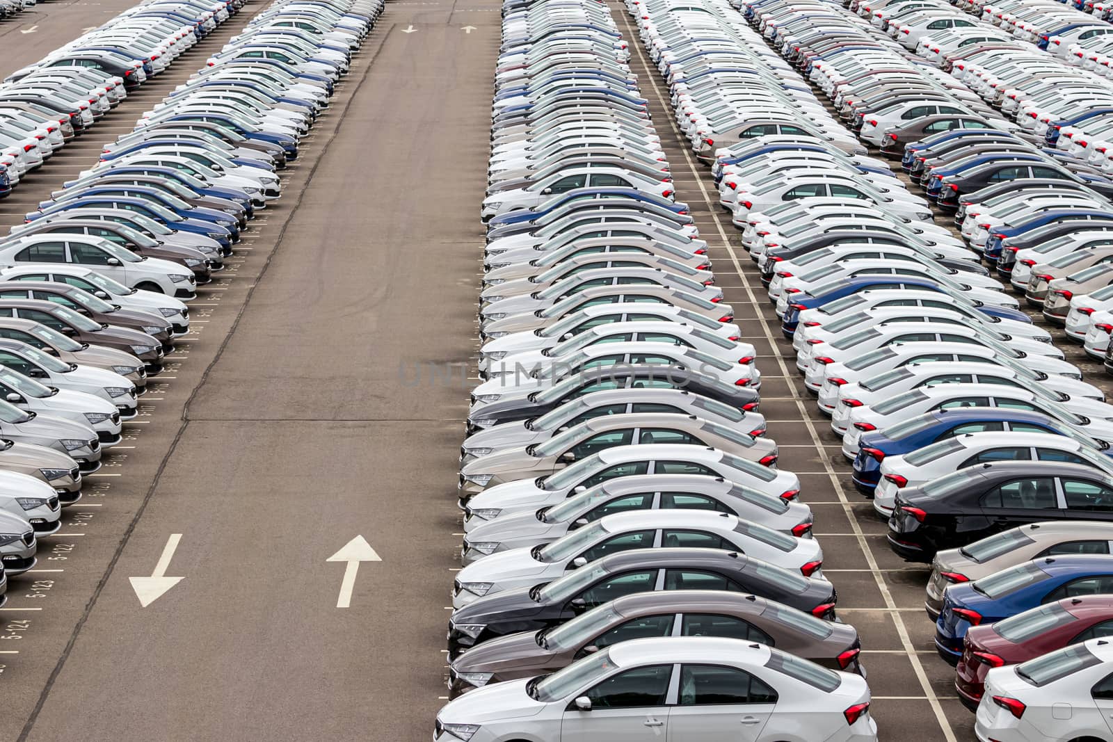 Rows of a new cars parked in a distribution center on a car factory on a cloudy day. Top view to the parking in the open air. by Eugene_Yemelyanov