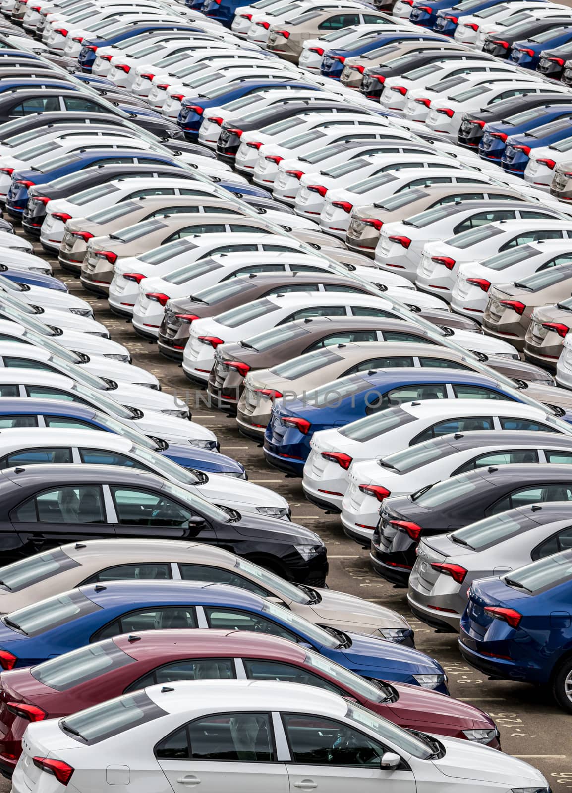 Rows of a new cars parked in a distribution center on a cloudy day in the spring, a car factory. Top view to the parking in the open air.