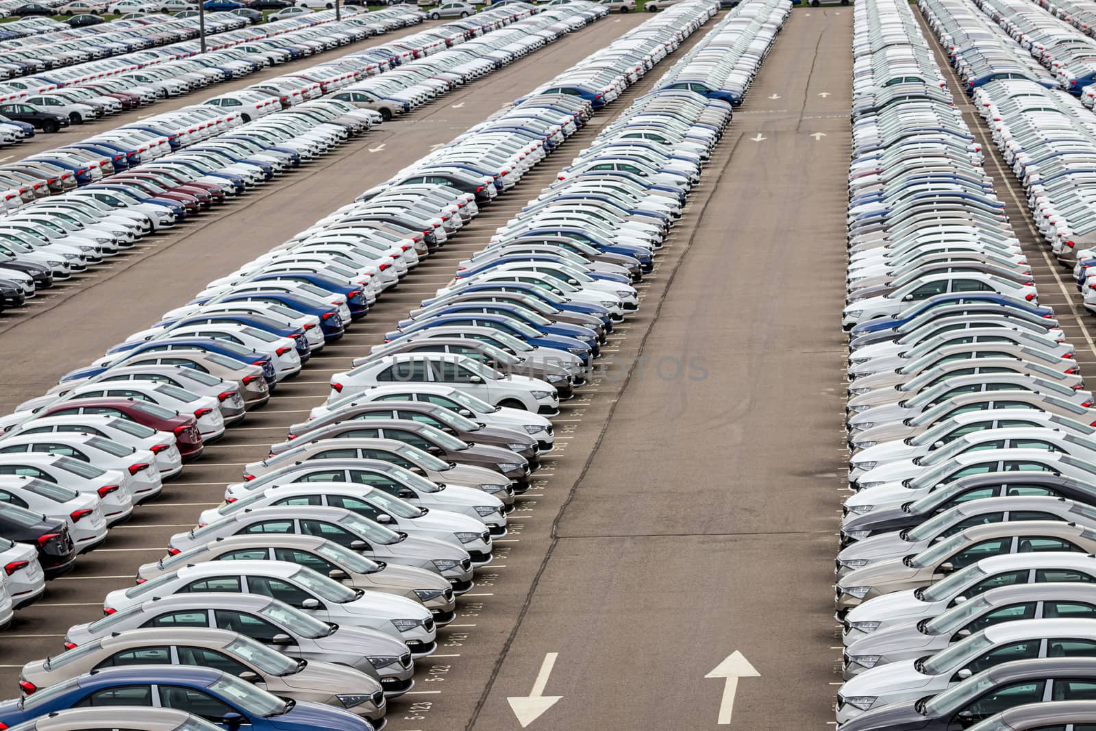 Rows of a new cars parked in a distribution center on a cloudy day in the spring, a car factory. Top view to the parking in the open air. by Eugene_Yemelyanov