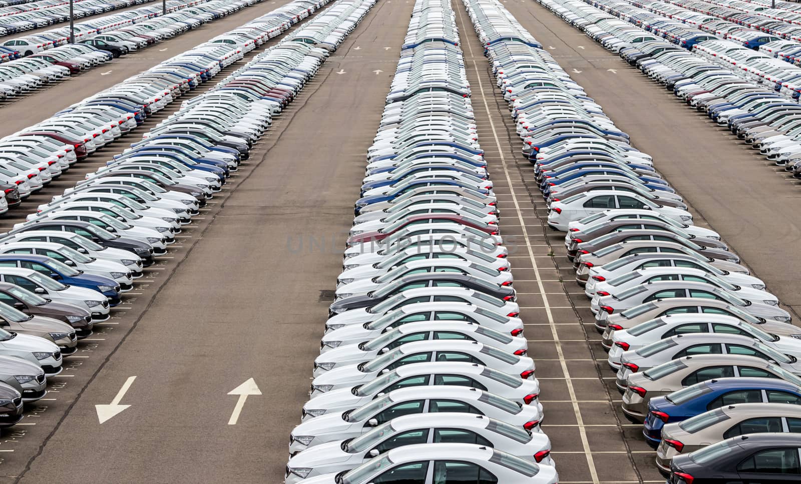 Rows of a new cars parked in a distribution center on a cloudy day in the spring, a car factory. Top view to the parking in the open air. by Eugene_Yemelyanov