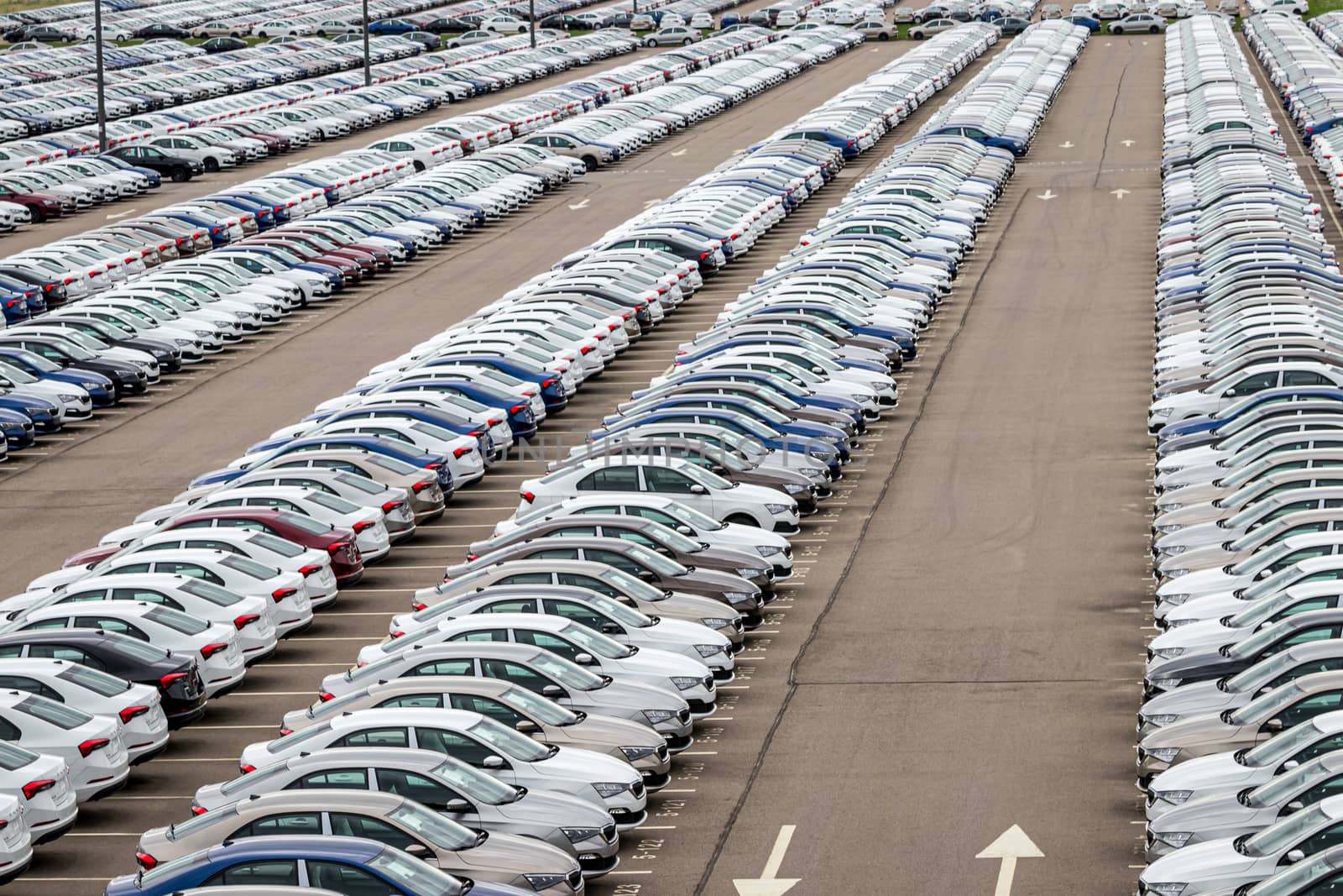 Rows of a new cars parked in a distribution center on a car factory on a cloudy day. Top view to the parking in the open air.