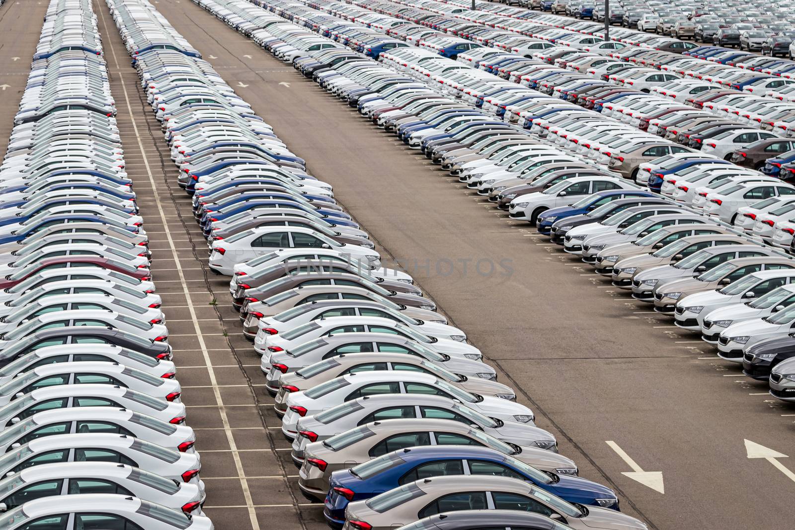 Rows of a new cars parked in a distribution center on a car factory on a cloudy day. Top view to the parking in the open air.