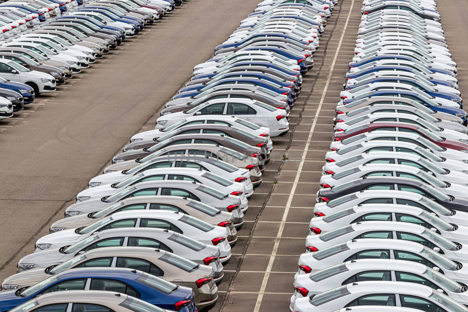 Rows of a new cars parked in a distribution center on a cloudy day in the spring, a car factory. Top view to the parking in the open air.