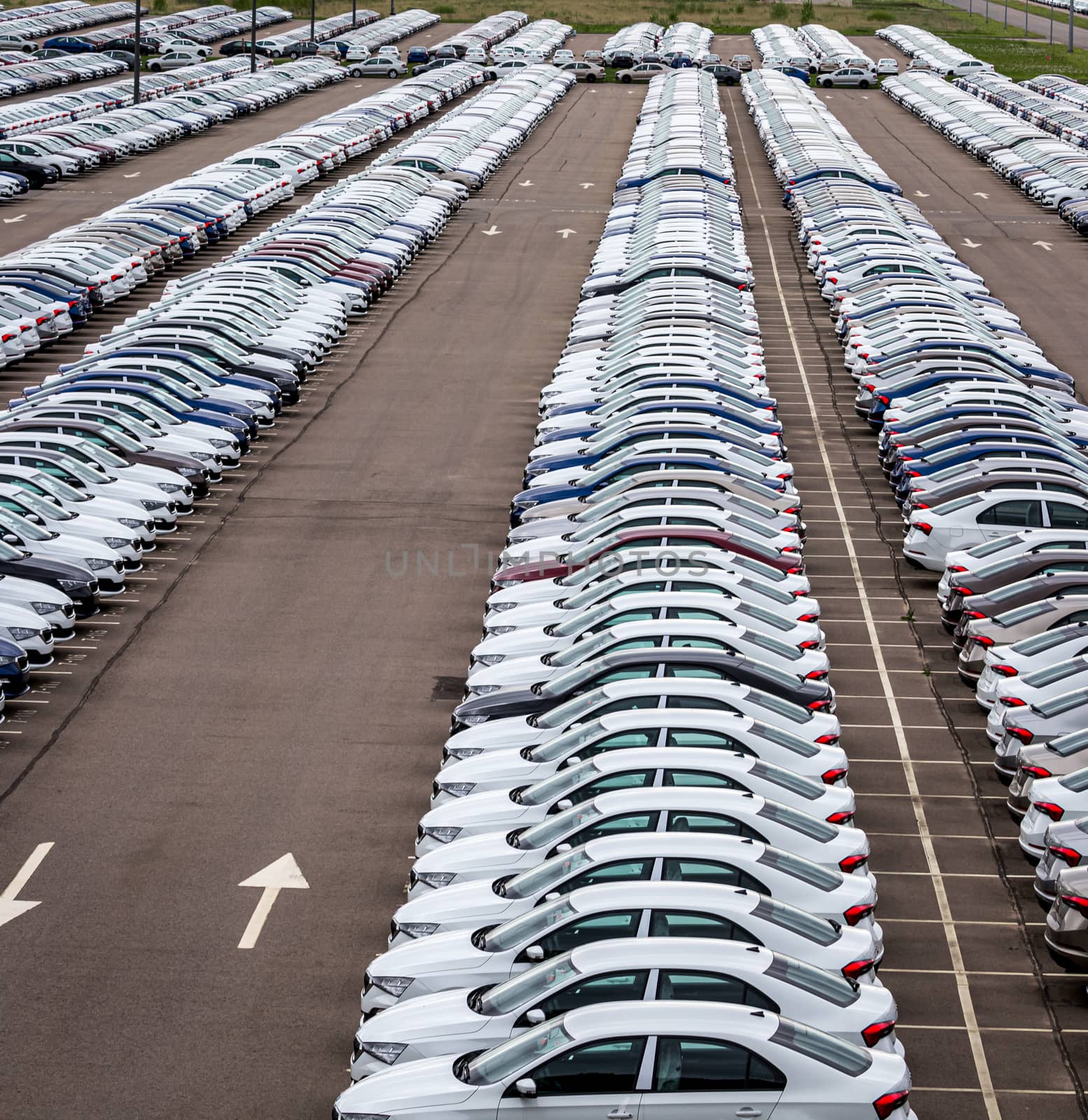 Rows of a new cars parked in a distribution center on a cloudy day in the spring, a car factory. Top view to the parking in the open air.