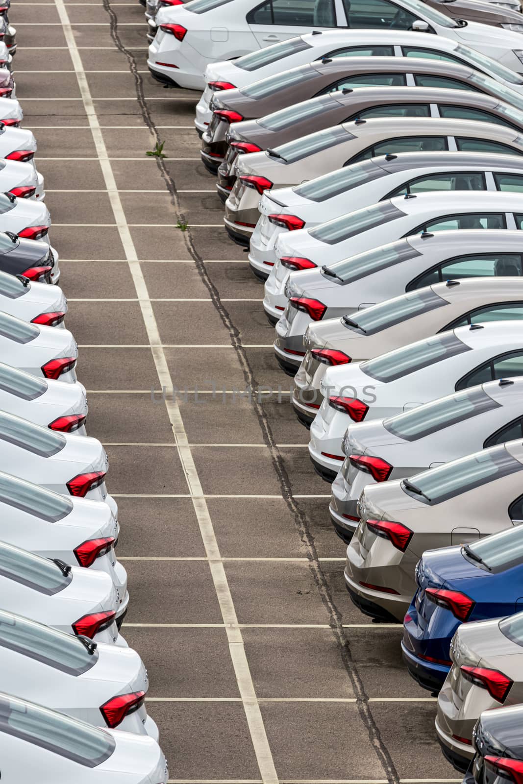 Rows of a new cars parked in a distribution center of a car factory. Top view to the parking in the open air.