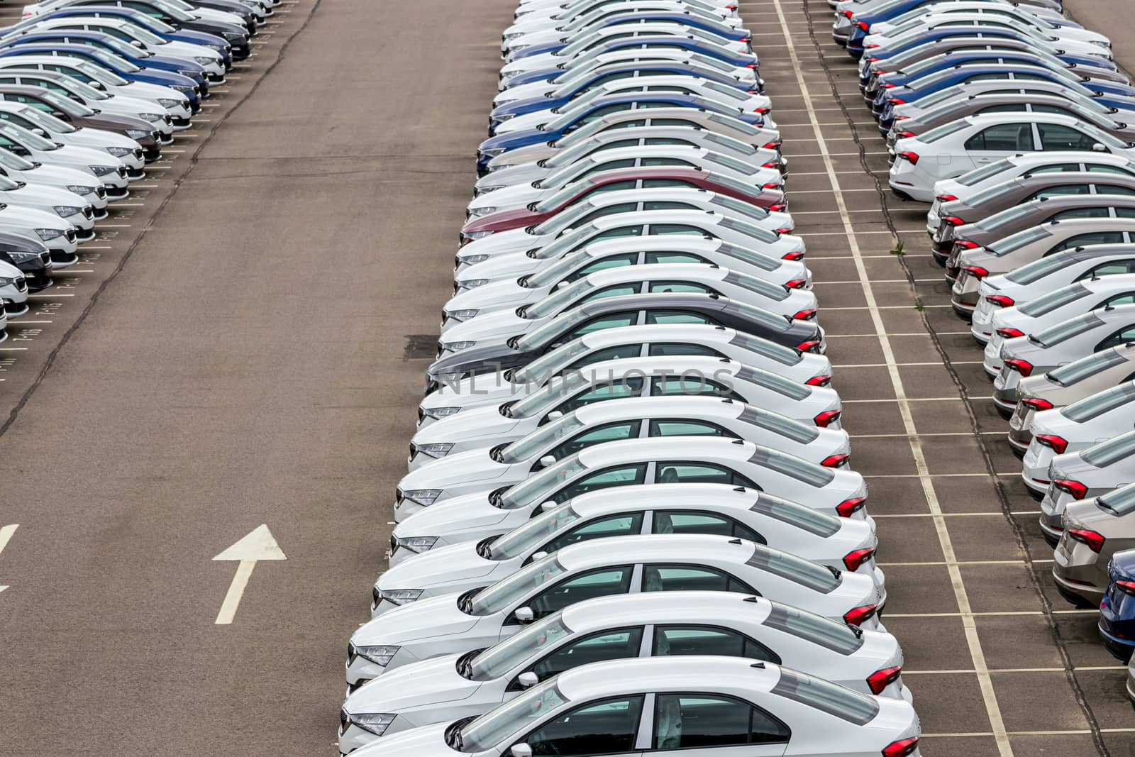 Rows of a new cars parked in a distribution center of a car factory. Top view to the parking in the open air. by Eugene_Yemelyanov