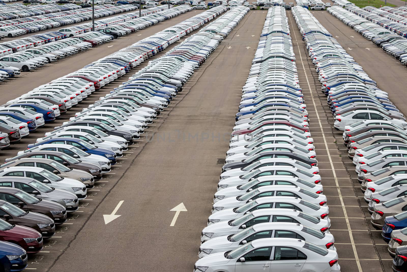 Rows of a new cars parked in a distribution center on a cloudy day in the spring, a car factory. Top view to the parking in the open air. by Eugene_Yemelyanov