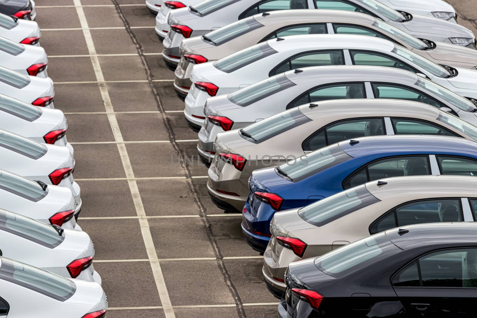 Rows of a new cars parked in a distribution center on a car factory on a cloudy day. Top view to the parking in the open air. by Eugene_Yemelyanov