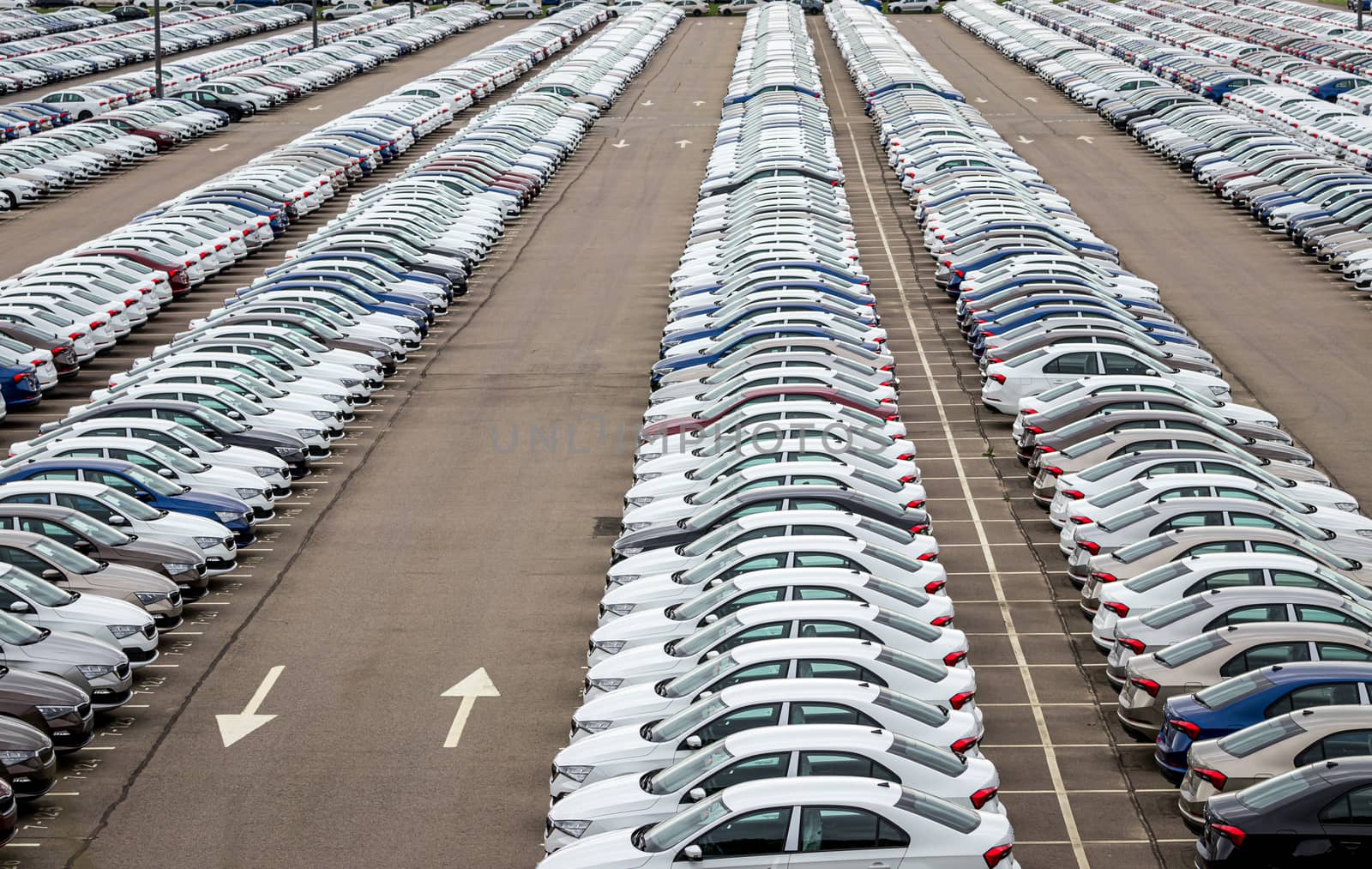 Rows of a new cars parked in a distribution center on a car factory on a cloudy day. Top view to the parking in the open air.