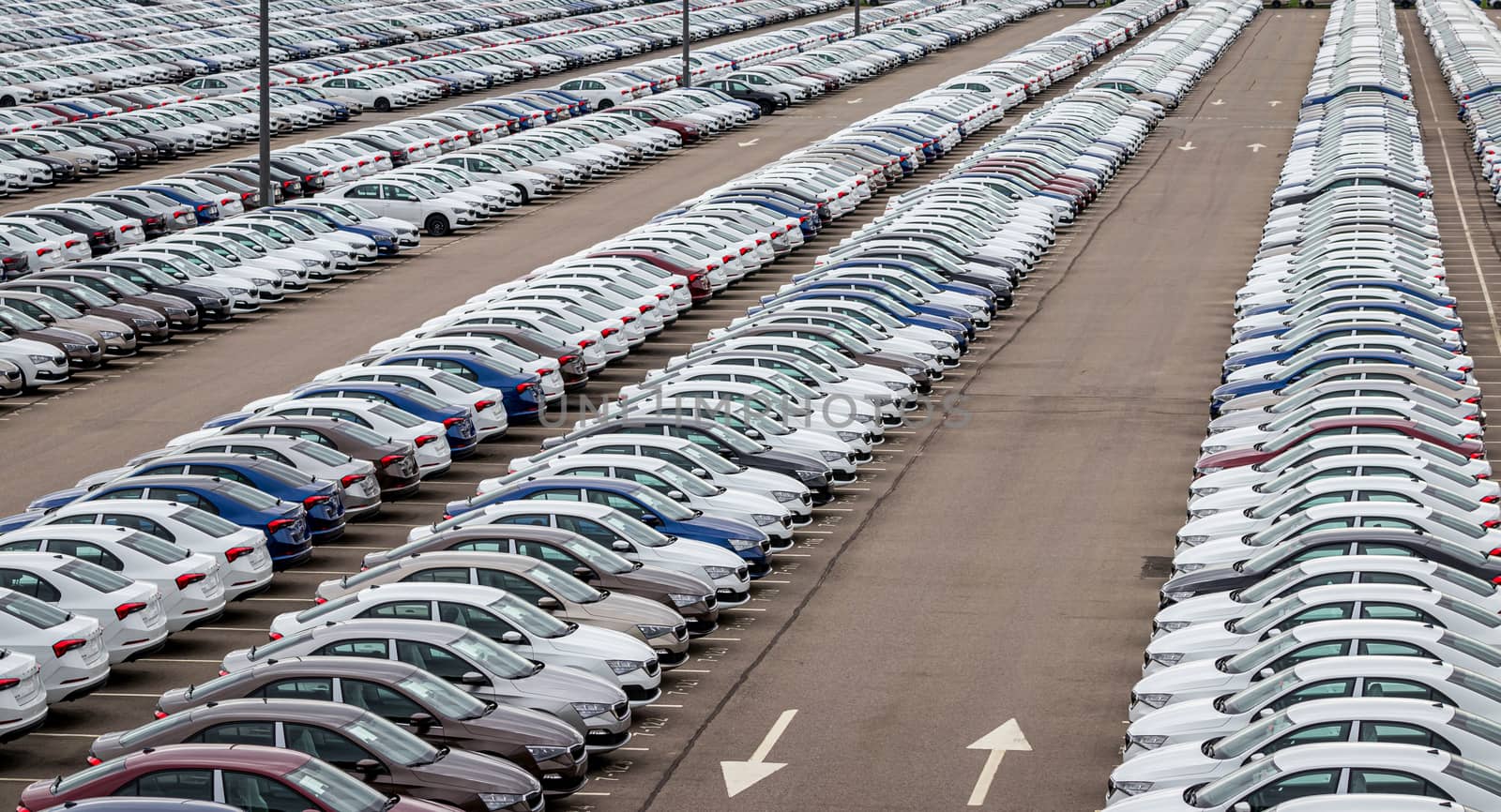 Rows of a new cars parked in a distribution center on a car factory on a cloudy day. Top view to the parking in the open air. by Eugene_Yemelyanov