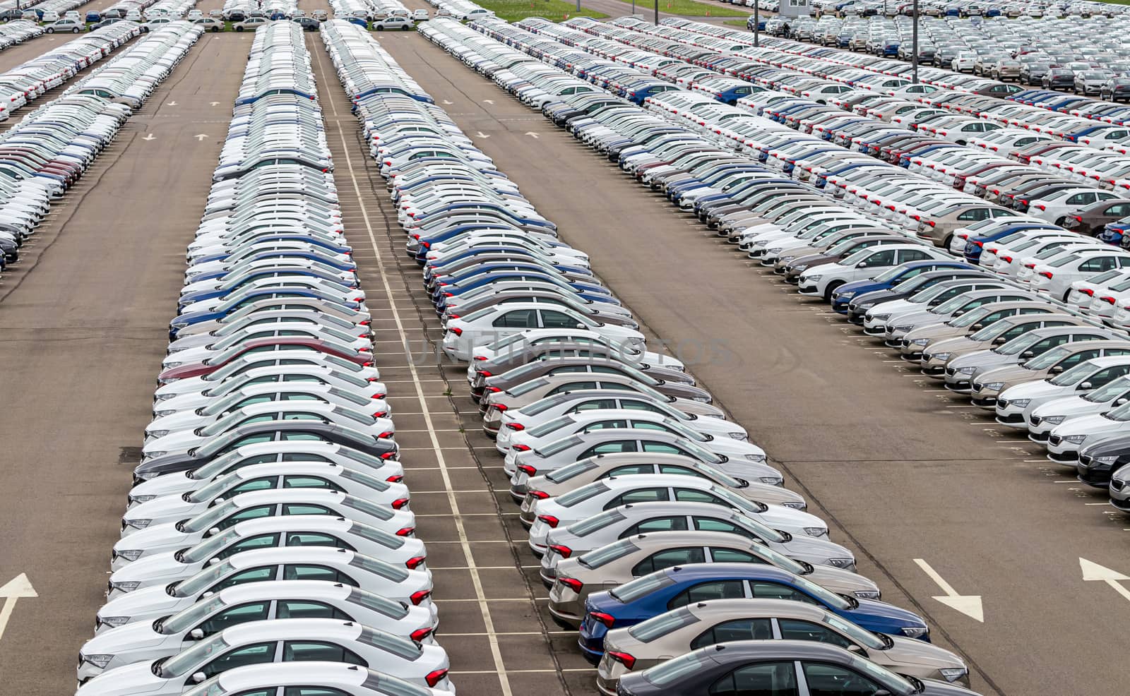 Rows of a new cars parked in a distribution center on a cloudy day in the spring, a car factory. Top view to the parking in the open air. by Eugene_Yemelyanov