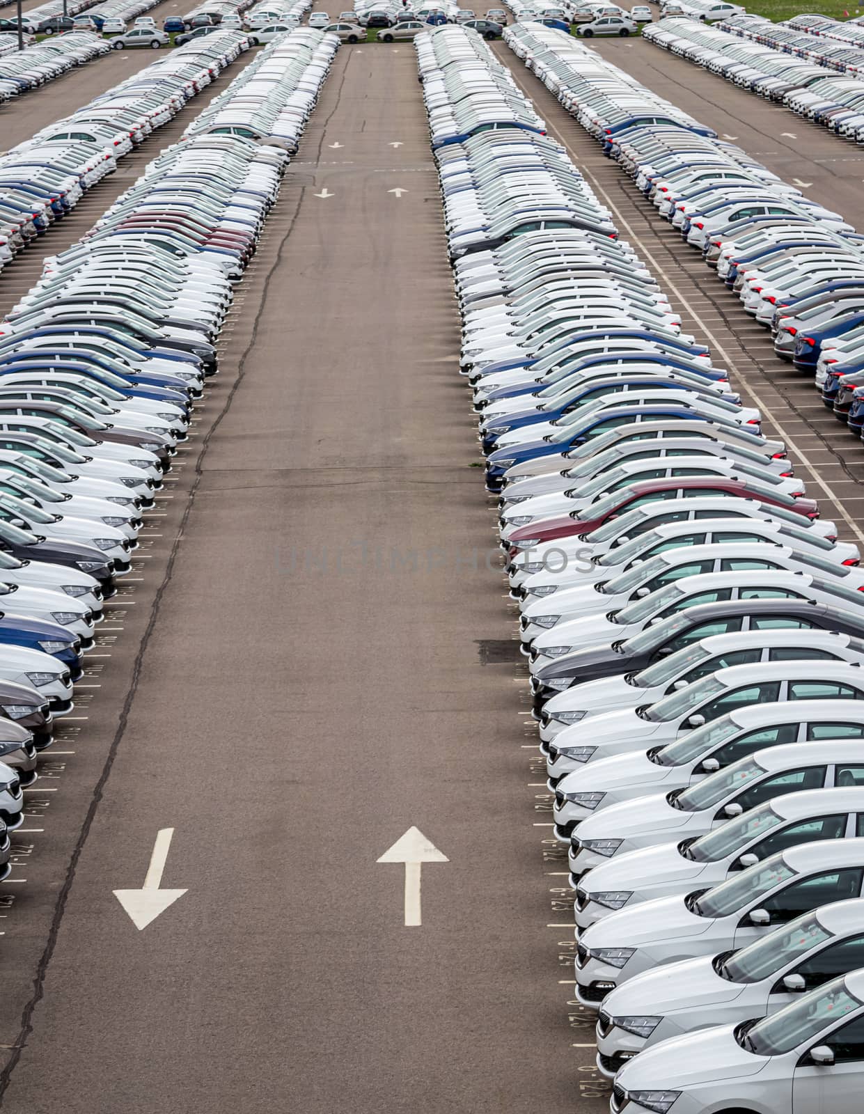 Rows of a new cars parked in a distribution center on a car factory on a cloudy day. Top view to the parking in the open air. by Eugene_Yemelyanov