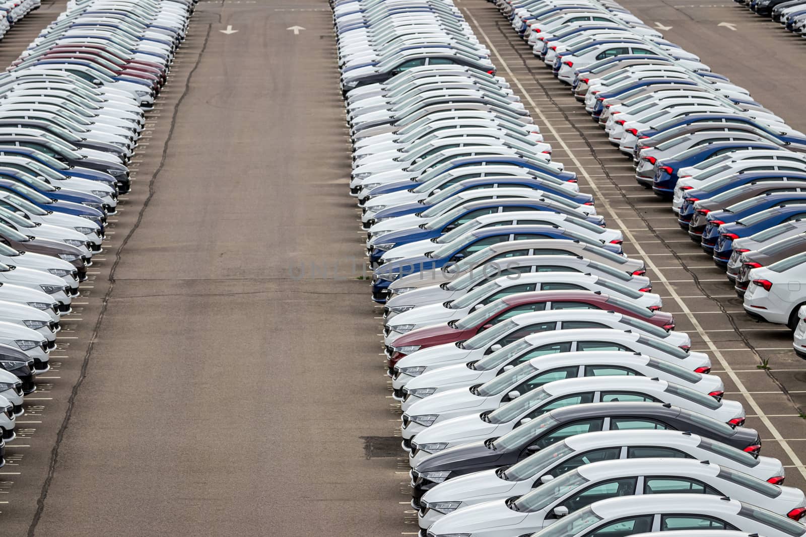 Rows of a new cars parked in a distribution center of a car factory. Top view to the parking in the open air.