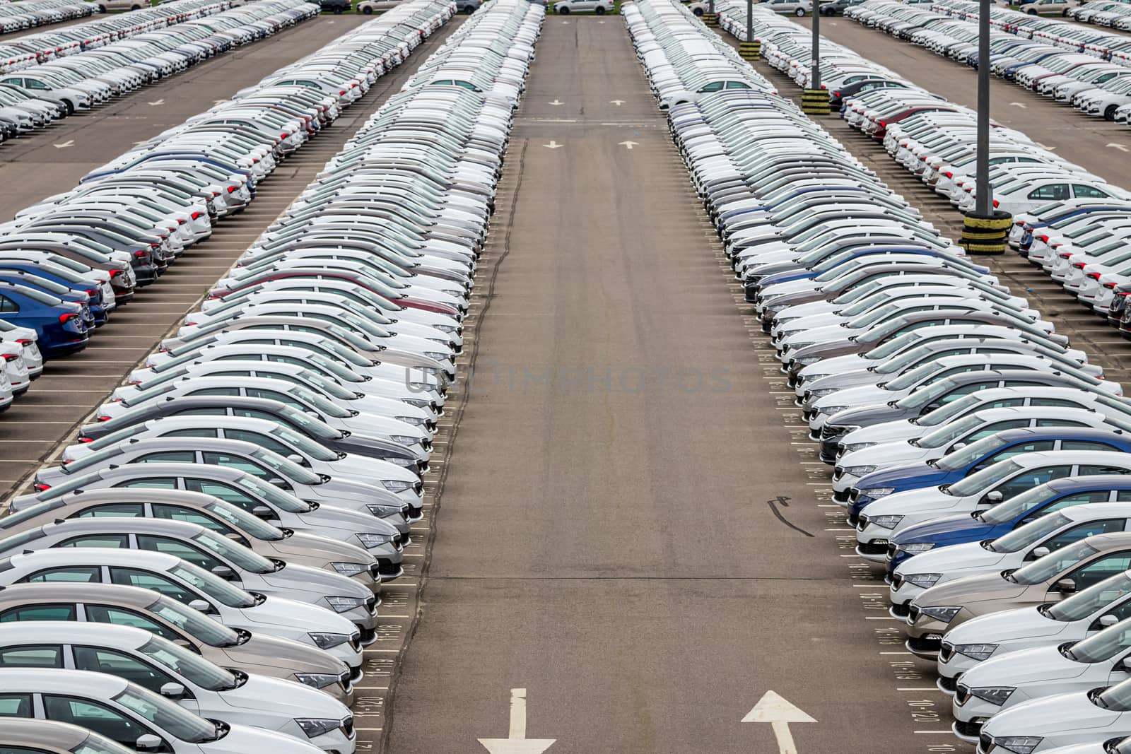 Rows of a new cars parked in a distribution center on a cloudy day in the spring, a car factory. Top view to the parking in the open air. by Eugene_Yemelyanov