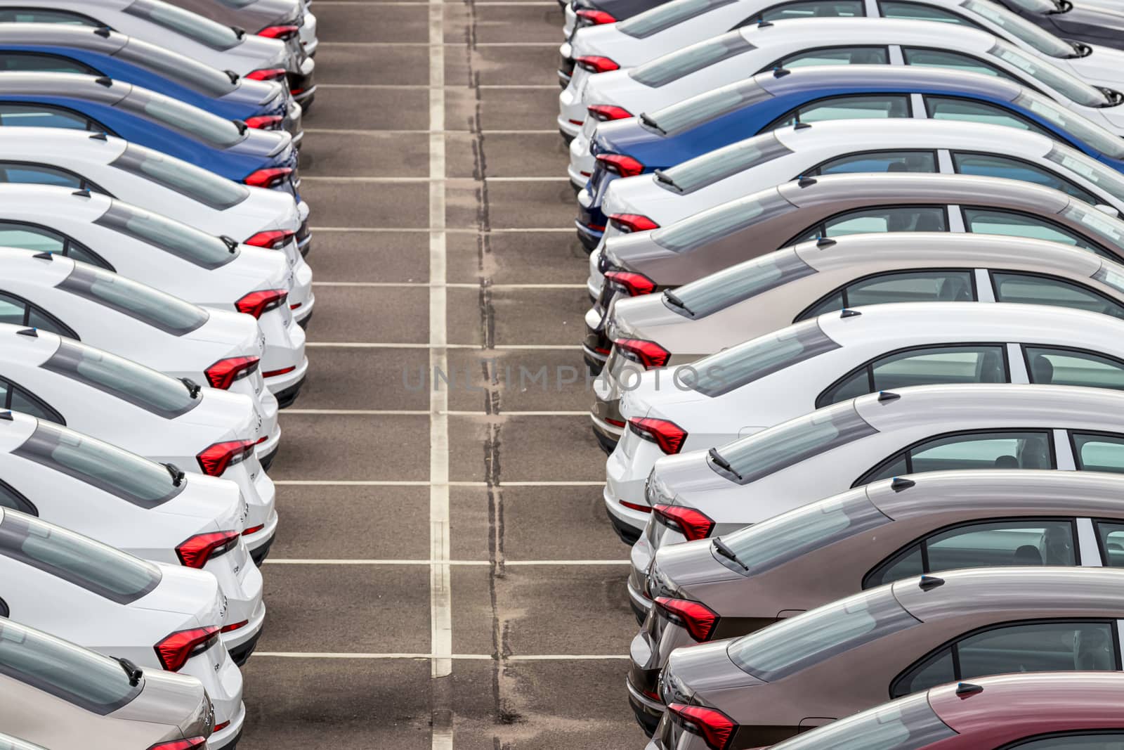 Rows of a new cars parked in a distribution center on a cloudy day in the spring, a car factory. Top view to the parking in the open air. by Eugene_Yemelyanov