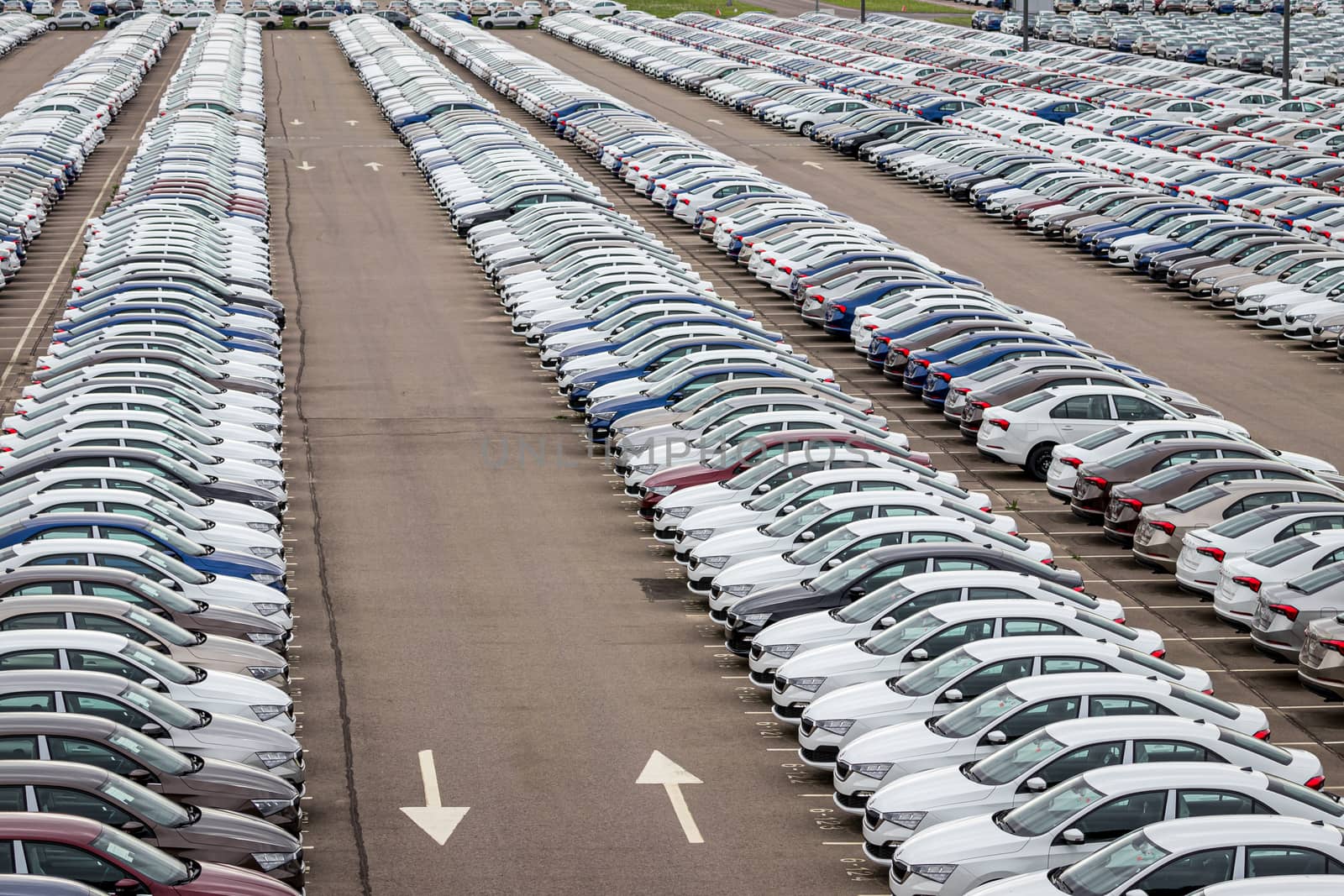 Rows of a new cars parked in a distribution center on a cloudy day in the spring, a car factory. Top view to the parking in the open air. by Eugene_Yemelyanov