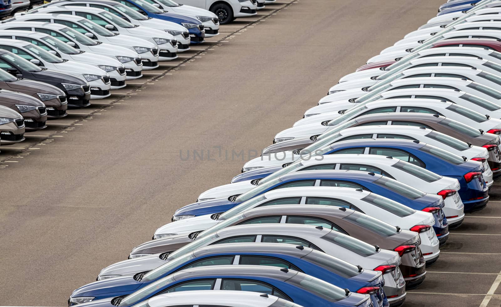 Rows of a new cars parked in a distribution center on a car factory on a cloudy day. Top view to the parking in the open air. by Eugene_Yemelyanov