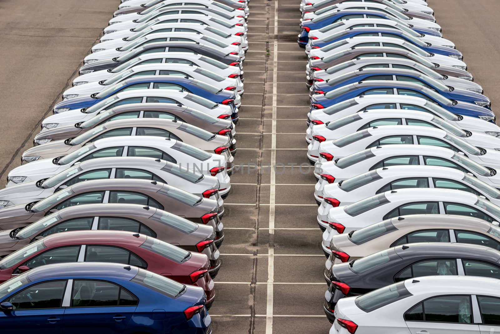 Rows of a new cars parked in a distribution center of a car factory. Top view to the parking in the open air. by Eugene_Yemelyanov